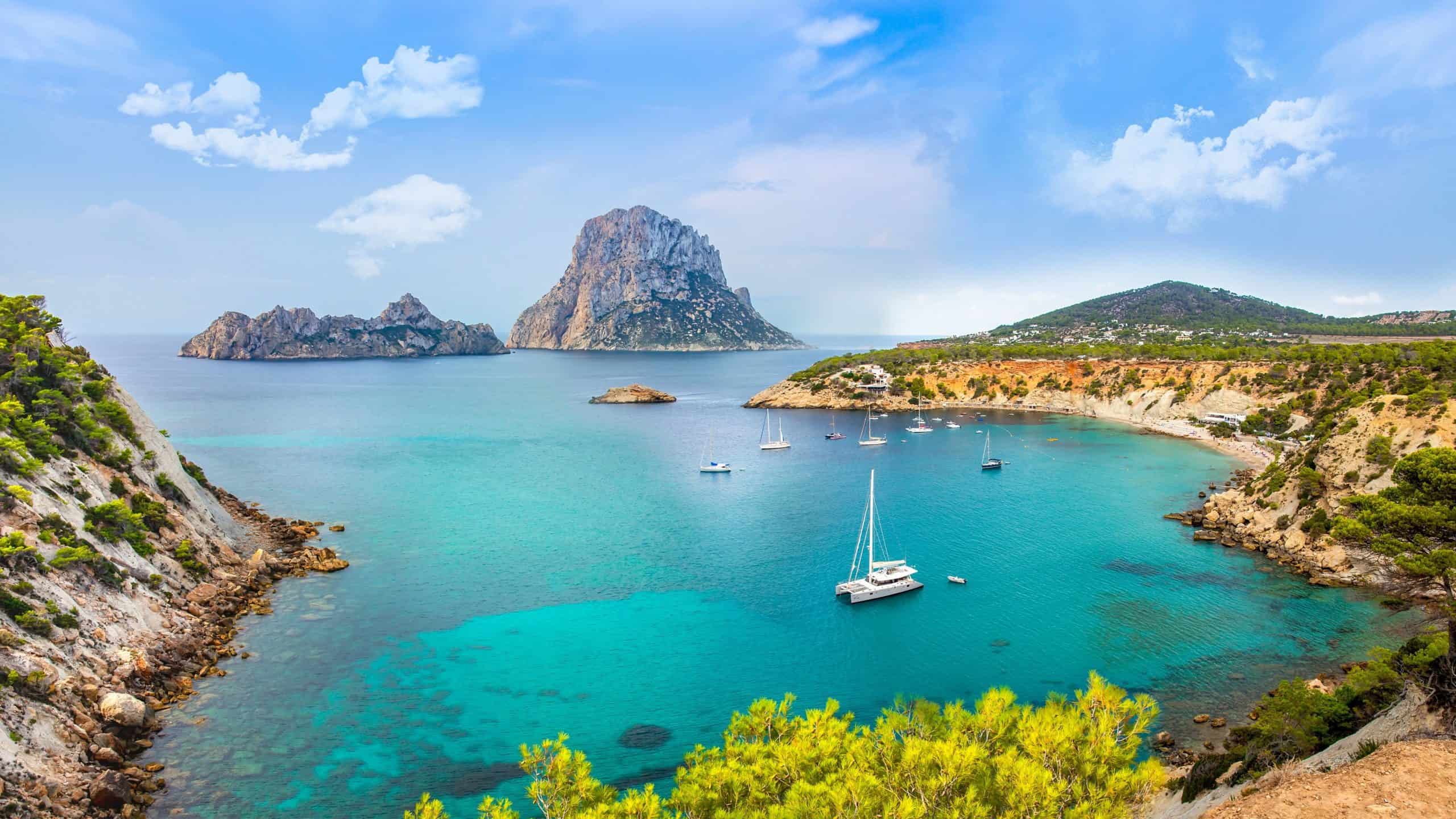 Picture of the gorgeous Ibiza(located in spain) landscape. Which shows mountains, crystal clear waters and boats