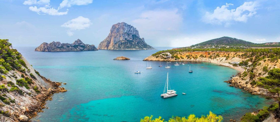 Picture of the gorgeous Ibiza(located in spain) landscape. Which shows mountains, crystal clear waters and boats